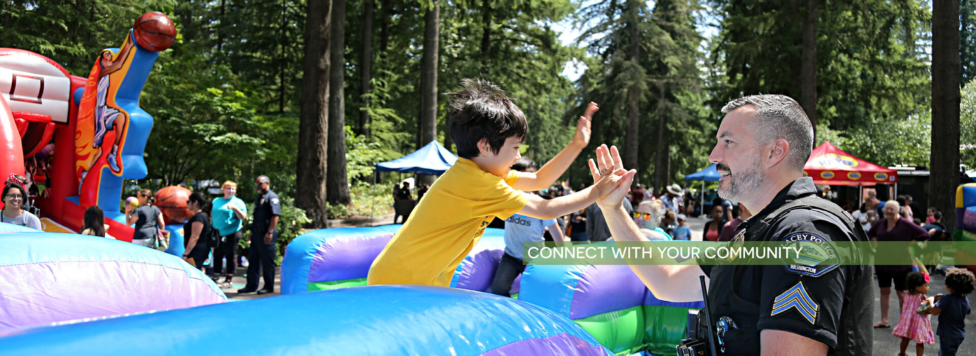 Child giving high five to police officer while jumping off of a bouncy house ride at the recent Cops for Kids event - click here to learn more about community events in Lacey